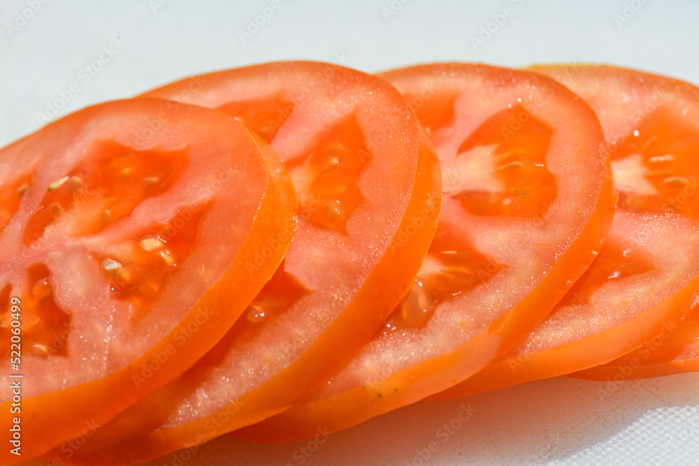 Close-up of fresh tomato slices arranged in a row on a white background