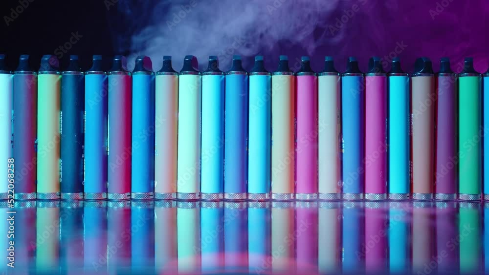 Lots of E-Cigarettes and Vapes with Smoke in Neon Lighting. Concept of Bad Habits. Modern Smoking Electronic Cigarettes. Slow Motion
