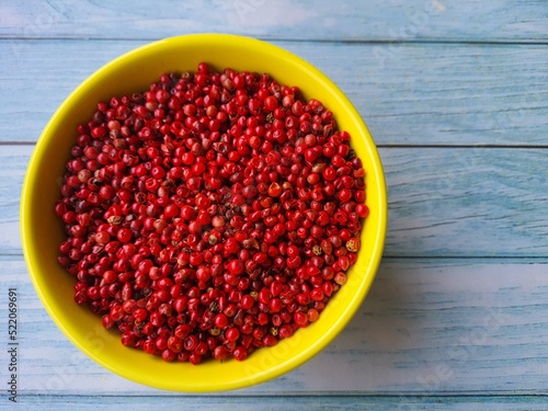 Pink pepper (Schinus terbinthifolia). In a yellow bowl isolated on a gray background. Selective focus. Also known as: Aroeira-Red, Aroeira-pimenteira or Poivre-rosa. photo