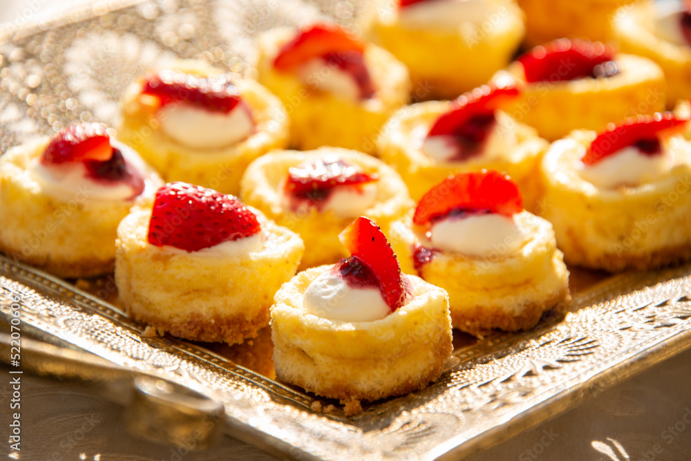 Rows of sweet tarts garnished with strawberries brightly lit on a tray for serving