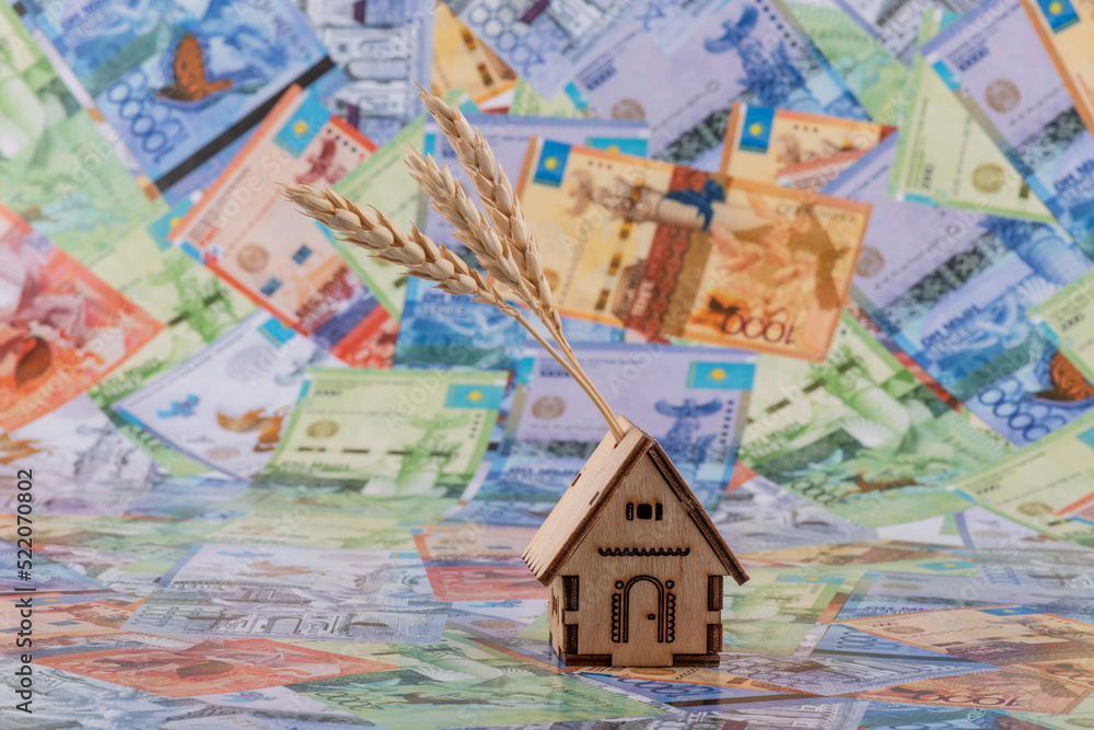 Symbolic wooden house and ears of wheat against the background of Kazakh banknotes - tenge