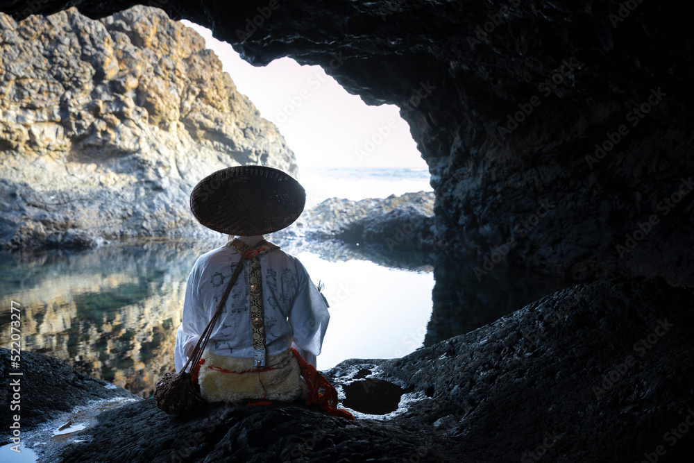Shugendo monk is sitting in cave and meditating while looking at open sea Shugendo monk is sitting in cave and meditating while looking at open sea