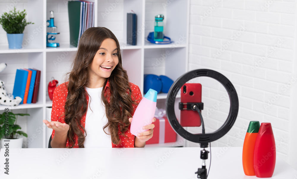 Teen girl blogger influencer use selfie led lamp and smartphone on tripod for making online video tutorial, hold hair conditioner or shampoo bottle. Teenager vlogger making vlog for kids channel. Teen girl blogger influencer use selfie led lamp and smartphone on tripod for making online video tutorial, hold hair conditioner or shampoo bottle. Teenager vlogger making vlog for kids channel.