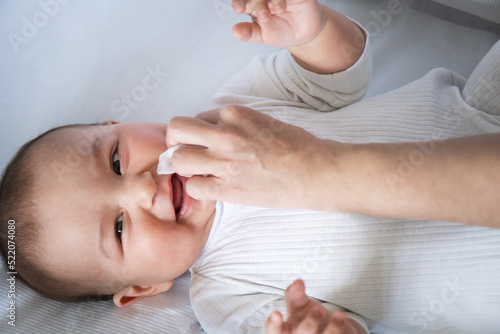 Mom wipes the baby's drool with a napkin. Baby care, teething, drooling. photo