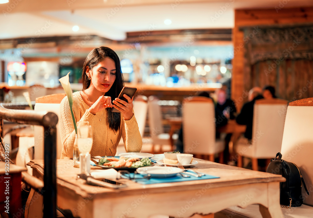 Fototapeta premium latin young woman sitting alone in a restaurant using smartphone .