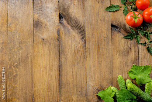 Wooden background. Fresh cucumbers, red tomatoes with leaves on a wooden background. Place for text. copy space.