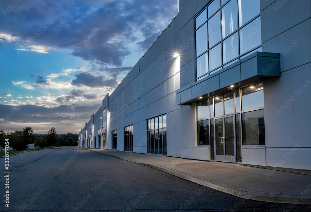 Exterior view of a generic business park building at dusk with multiple high bay units, prefab metal cladding, glazing, aluminum mullions, exterior lights on, nobody - obrazy, fototapety, plakaty 