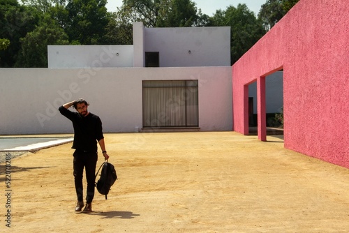 Fashionable man dressed in black with a backpack standing by an architectural work of Luis Barragan photo