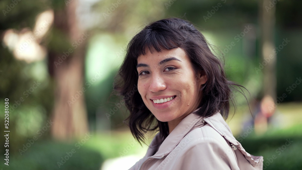 Happy South American young woman portrait face smiling at camera standing outside. Young latin person in 20s. Tracking shot in motion Happy South American young woman portrait face smiling at camera standing outside. Young latin person in 20s. Tracking shot in motion