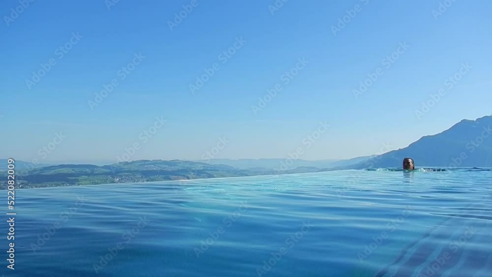 Woman Swimming and Enjoy Infinity Swimming Pool with View over Mountain and Lake Lucerne in a Sunny Summer Day in Burgenstock, Nidwalden, Switzerland. Woman Swimming and Enjoy Infinity Swimming Pool with View over Mountain and Lake Lucerne in a Sunny Summer Day in Burgenstock, Nidwalden, Switzerland.