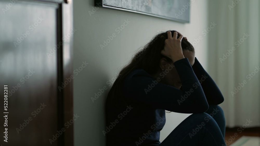 Woman feeling emotional pain sitting on floor home being desperate covering face with shame Woman feeling emotional pain sitting on floor home being desperate covering face with shame
