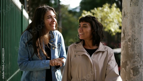 Women speaking while walking in street. Two girlfriends chatting in conversation in urban city sidewalk