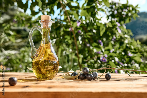 Foto Extra virgin olive oil and olive branch in the bottle on wooden table in the olive grove