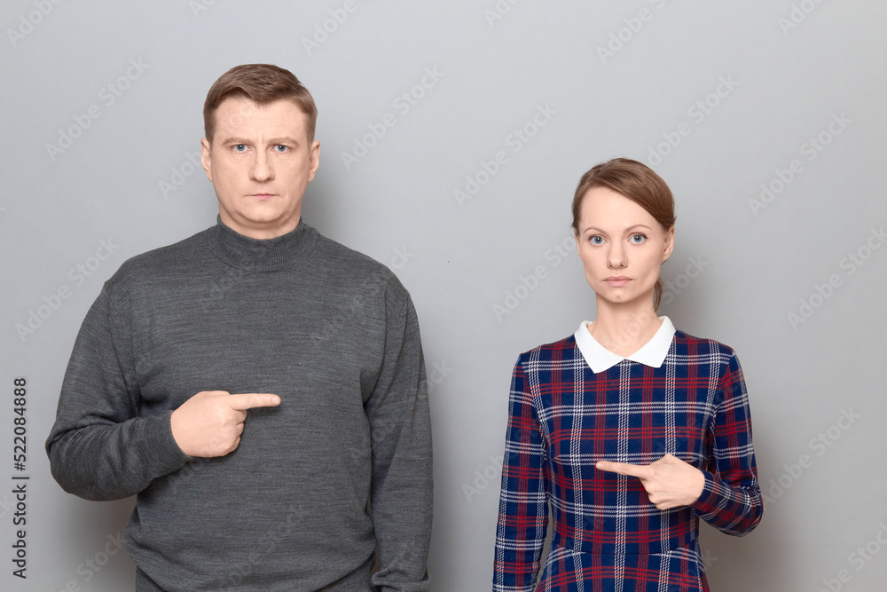 Studio shot of man and woman pointing with index fingers at each other Studio shot of man and woman pointing with index fingers at each other