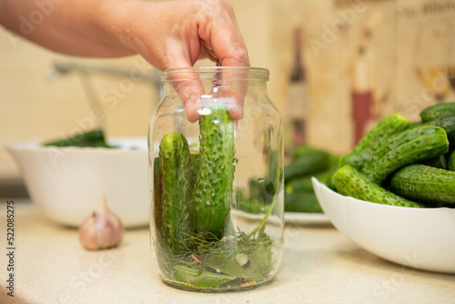 A woman puts cucumbers in a canning jar
