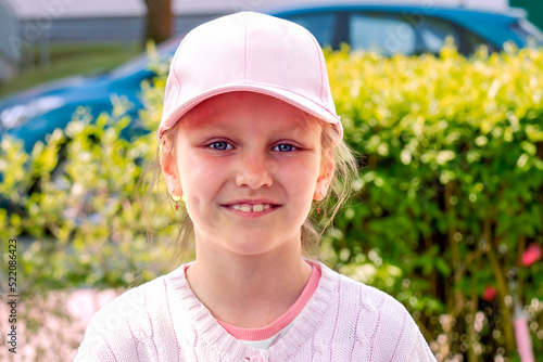 close-up portrait of a little cheerful girl 7-8 years old, in a baseball cap, against the background of a summer landscape