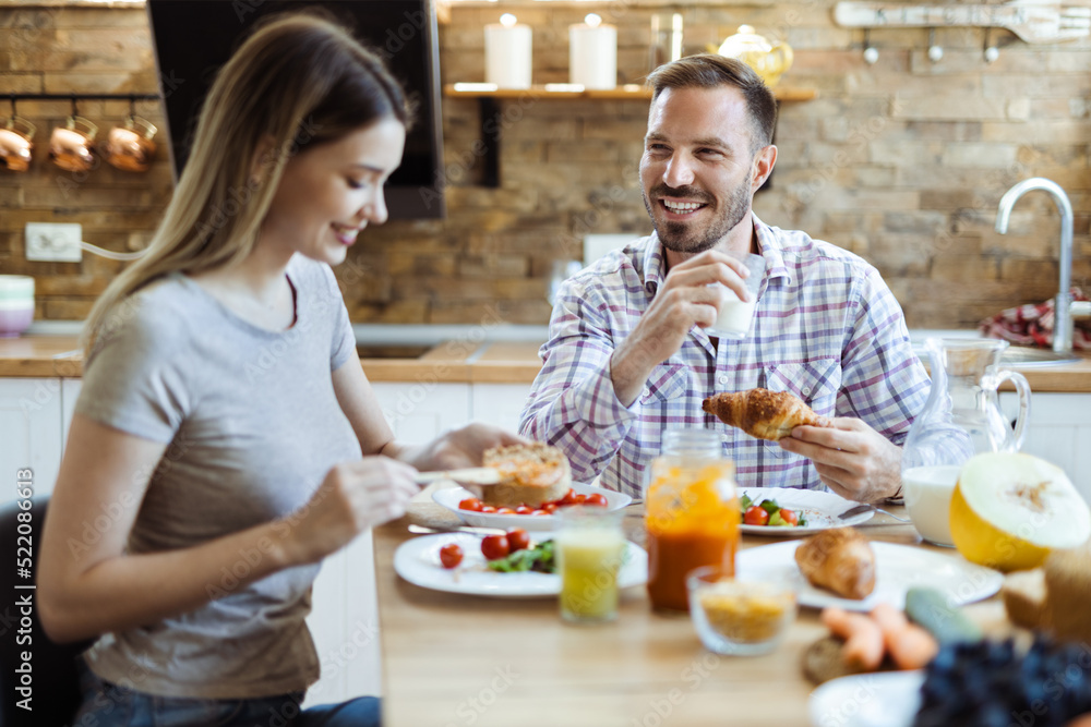 Happy young couple talking while enjoying in their breakfast at home