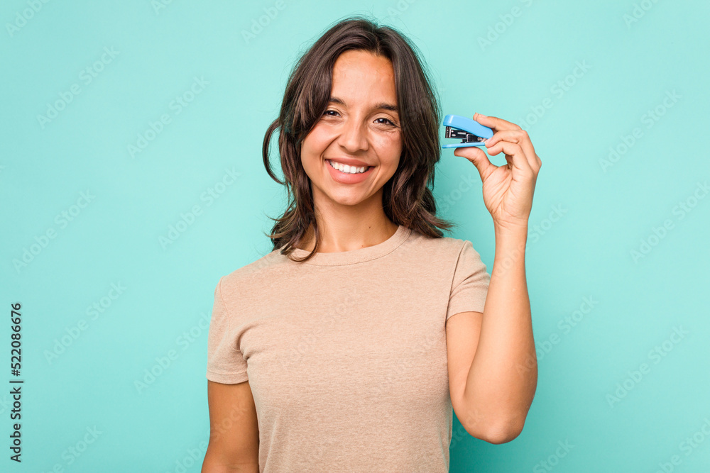 Young hispanic woman holding stapler isolated on blue background laughing and having fun. Young hispanic woman holding stapler isolated on blue background laughing and having fun.