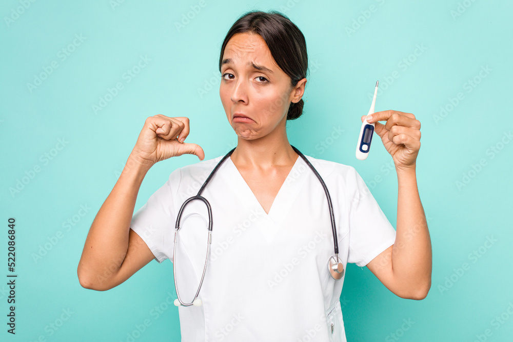 Young hispanic nurse woman holding a thermometer isolated on blue background feels proud and self confident, example to follow. Young hispanic nurse woman holding a thermometer isolated on blue background feels proud and self confident, example to follow.