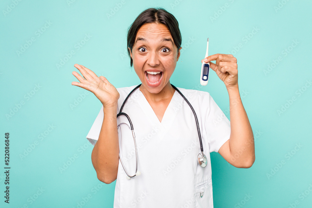 Young hispanic nurse woman holding a thermometer isolated on blue background surprised and shocked. Young hispanic nurse woman holding a thermometer isolated on blue background surprised and shocked.