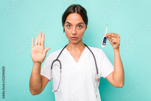 Young hispanic nurse woman holding a thermometer isolated on blue background standing with outstretched hand showing stop sign  preventing you.