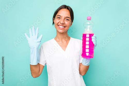 Young cleaner hispanic woman isolated on blue background smiling cheerful showing number five with fingers.
