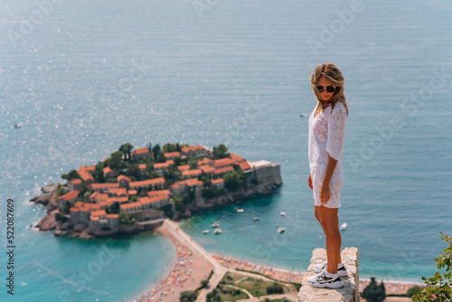 a girl poses on a mountain with a top view of the city of Sveti Stefan in Montenegro, a picturesque bay