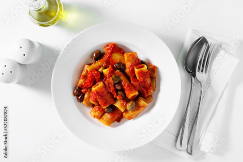 Fototapeta Naklejka Na Ścianę i Meble -  Italian tortiglioni pasta puttanesca with tomato sauce and black olives on the white table serving on the table with cutlery