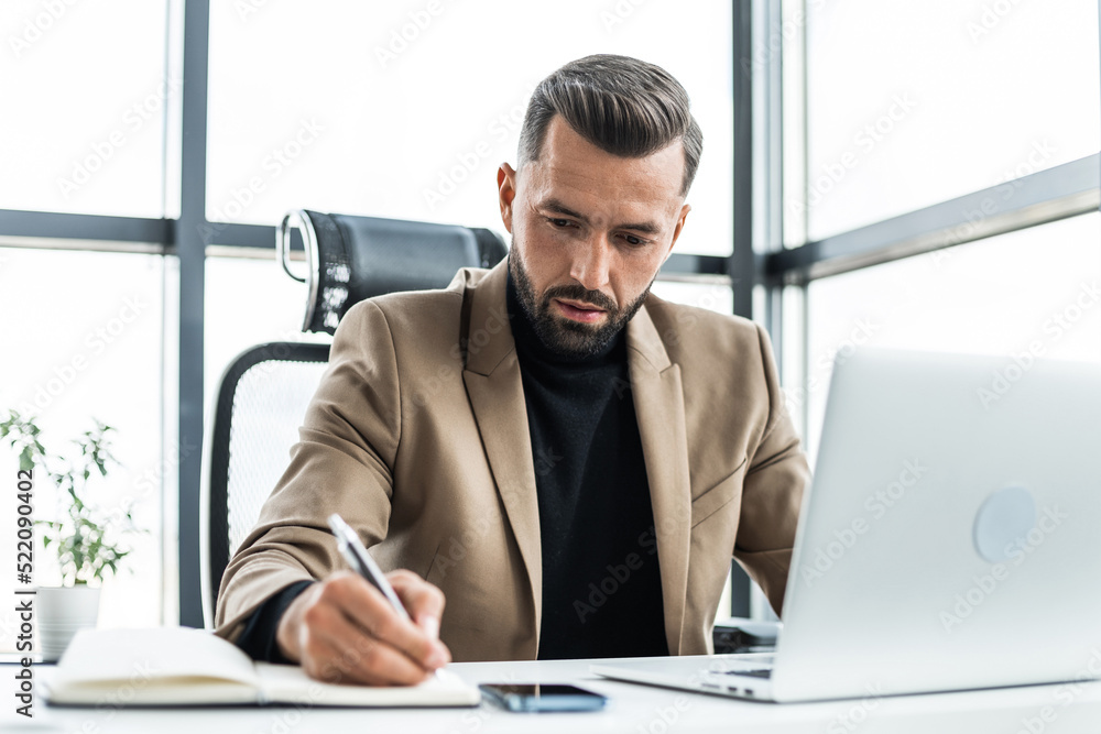 Fototapeta premium A concentrated businessman writes in a notebook sitting in an office