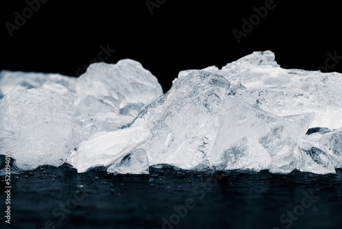 Natural ice cubes background. Heap of natural crushed ice on the black reflective surface on black background.