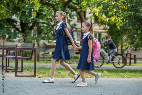 Fototapeta Naklejka Na Ścianę i Meble -  Two schoolgirls go to school with backpacks. Concept back to school, learning, friendship