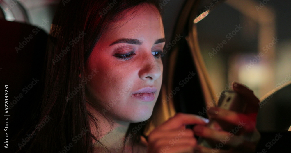 Passenger girl in the back seat of a car typing on her cellphone at night