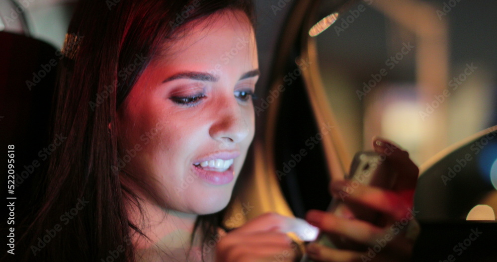 Fototapeta premium Passenger girl in the back seat of a car typing on her cellphone at night