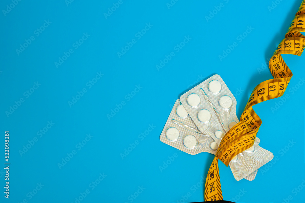 Tablets in plates wrapped with centimeter tape on a blue background. the plates are narrowed in middle, forming a waist or hourglass. concept of weight loss, fat burner, vitamins, sports nutrition. - obrazy, fototapety, plakaty 