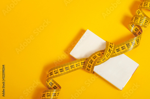 package of tablets with a white surface wrapped with a centimeter tape on a yellow background. The concept of weight loss, fat burner, vitamins, sports nutrition.