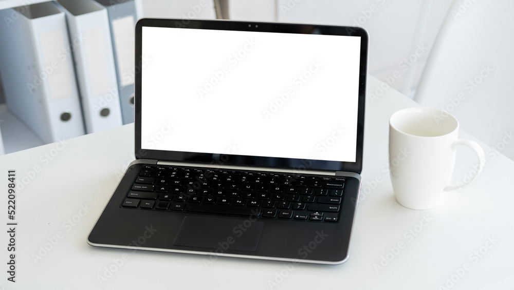Online technology. Computer mockup. Distance work. Opened laptop with blank screen staying on desk with cup of coffee in light room interior. Online technology. Computer mockup. Distance work. Opened laptop with blank screen staying on desk with cup of coffee in light room interior.