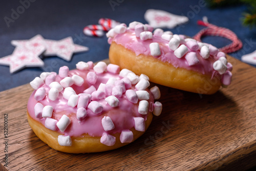 Pink glazed doughnut and marshmallow with Christmas decorations on a wooden cutting board