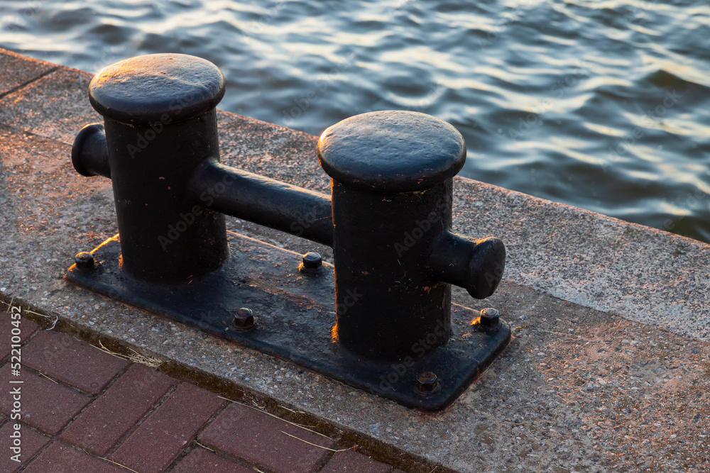 Black coastal bollard is on a concrrete pier, close up Black coastal bollard is on a concrrete pier, close up