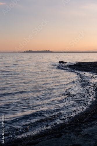 Shore of Trasimeno lake Umbria  Italy with Castiglione del Lago town at the distance at sunset