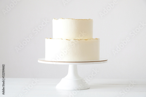 Cake with white cream, decorated with gold confectionery sprinkles on a white background. Two-tiered white wedding cake. photo