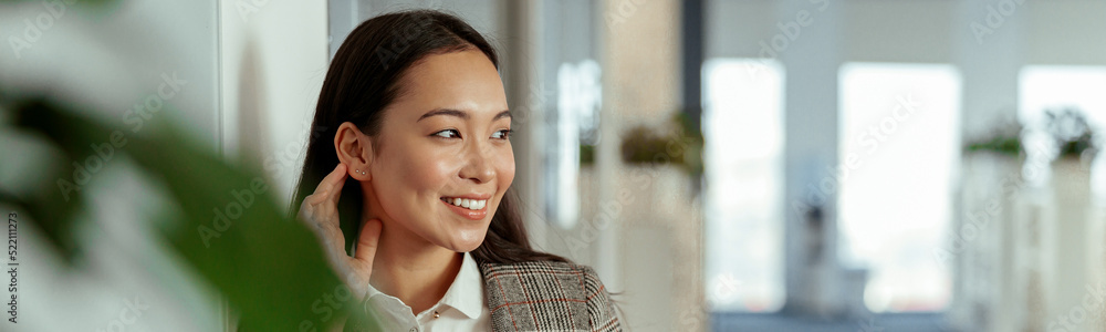 Charming Asian woman with a smile holding mobile phone at the office and looking away Charming Asian woman with a smile holding mobile phone at the office and looking away