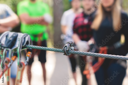 View of high ropes course, process of climbing in amusement acitivity rope park, passing obstacles and zip line on heights in climbing safety equipment gear between the trees, summer sunny day © tsuguliev
