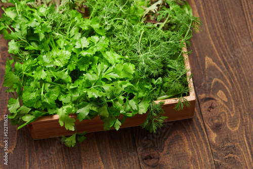 a top of bunch of green dill, parsley, salad, herbs and other greens in a wooden box, dark wood background, concept of fresh vegetables and healthy food