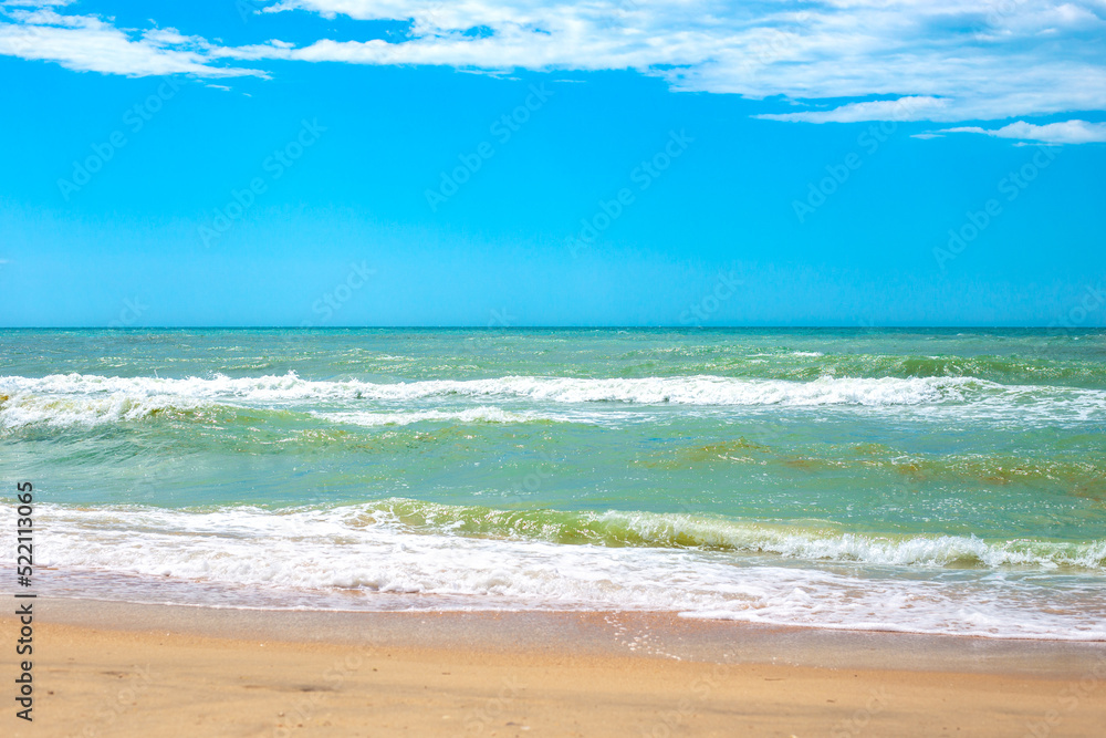 Sea with waves and sandy shore, blue sky on the horizon. Travel and tourism