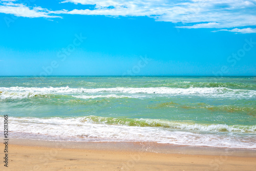 Sea with waves and sandy shore, blue sky on the horizon. Travel and tourism