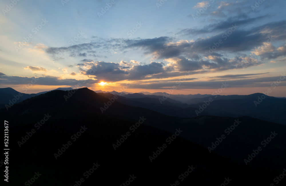 Beautiful evening landscape. Coniferous forest covers mountain hills. Forested hills in rising fog. Mountain sunset hills. Breathtaking aerial view of the tall mountains covered by the forest. Beautiful evening landscape. Coniferous forest covers mountain hills. Forested hills in rising fog. Mountain sunset hills. Breathtaking aerial view of the tall mountains covered by the forest.