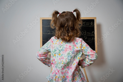 Little girl pupil at school at the blackboard solves mathematical task. Back view. Preparing to school. Ready to school concept.