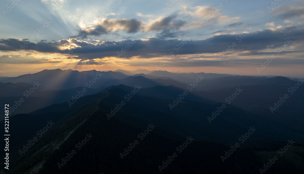 Beautiful evening landscape. Coniferous forest covers mountain hills. Forested hills in rising fog. Mountain sunset hills. Breathtaking aerial view of the tall mountains covered by the forest. 
