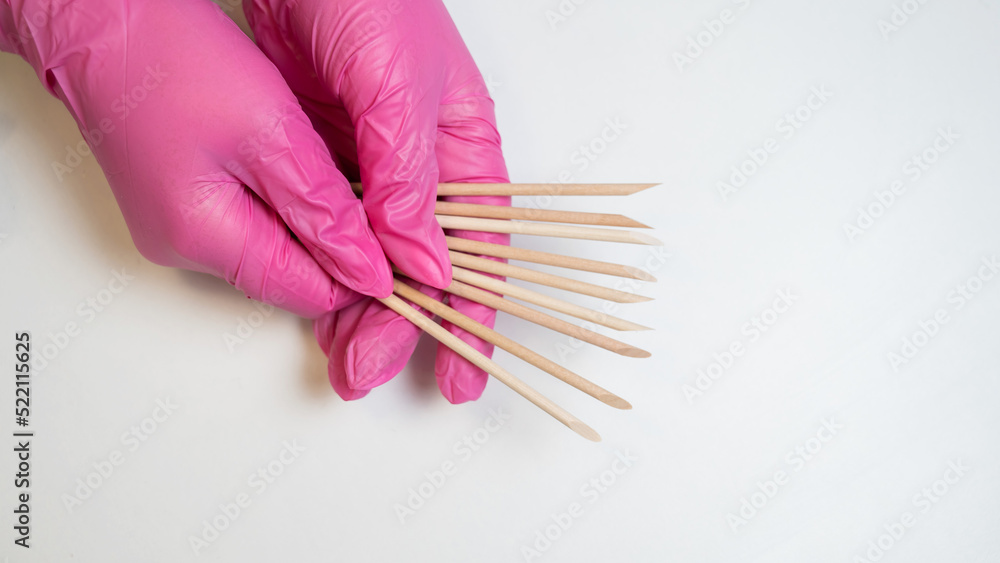 Master in pink gloves holds orange sticks for manicure. Master in pink gloves holds orange sticks for manicure.