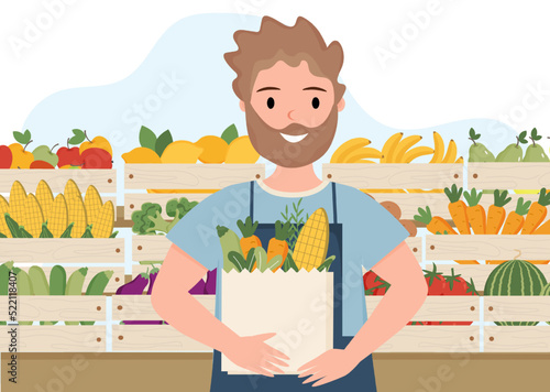 Young man shop assistant in fruit and vegetable shop. Male shop assistant is standing near counter with bag in his hands. Farmer is selling fruits and vegetables Young man is selling organics product